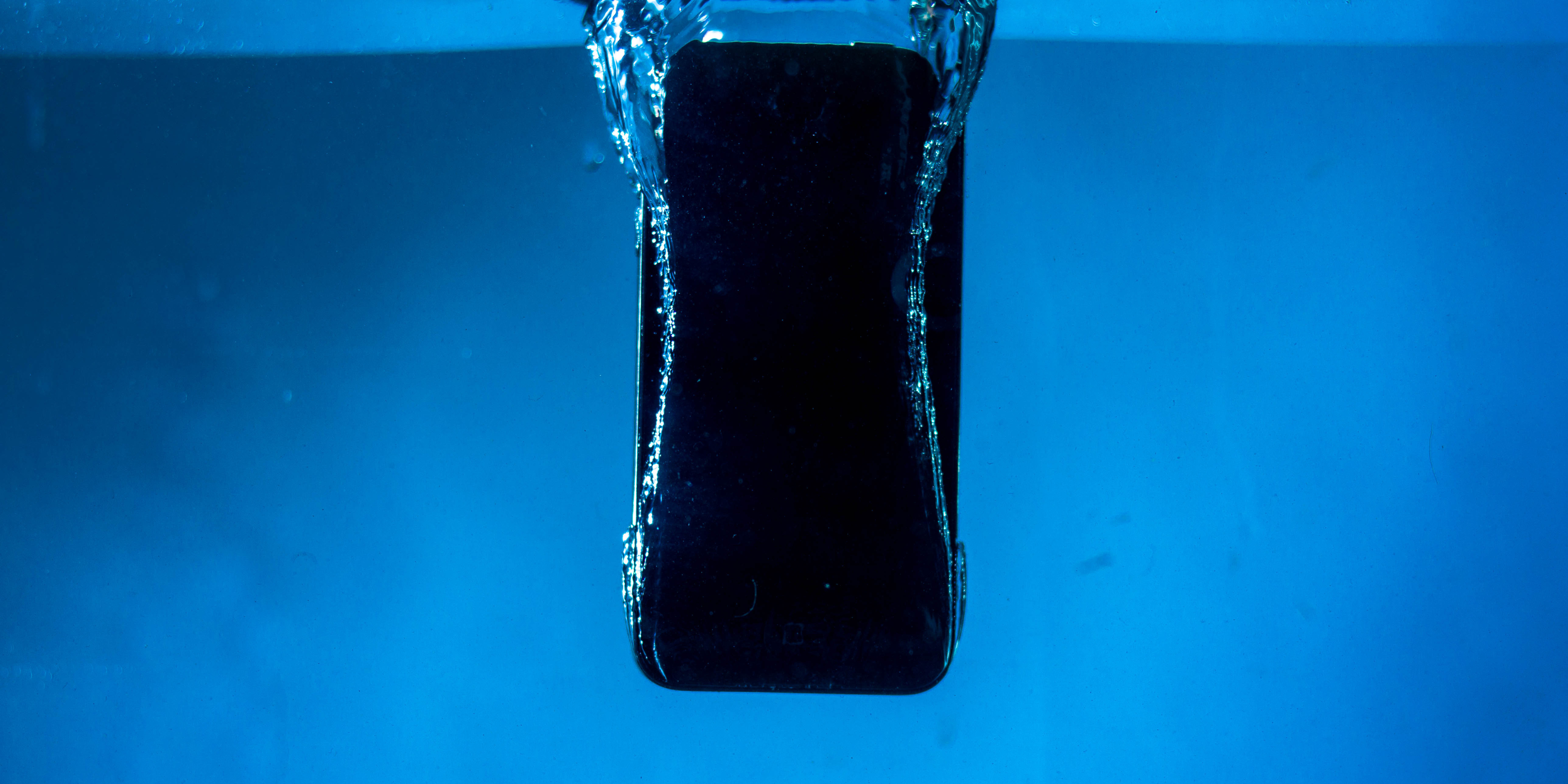 A high-speed photograph of a smartphone mid-plunge into a body of water, with a splash of water droplets frozen in the air.